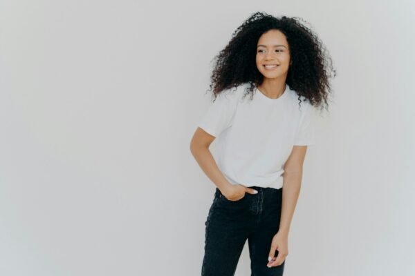 lady has slim figure, wears white t shirt and jeans, looks aside with happy expression